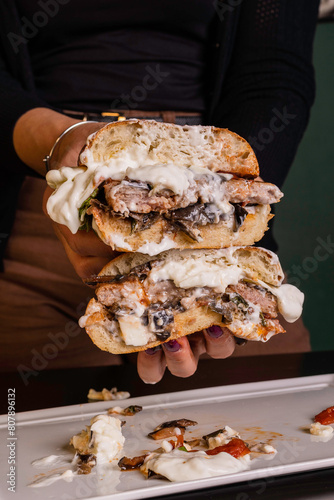 Panino da pub ripieno di hamburger di manzo, melanzane a funghetto, basilico fresco e burrata pugliese tagliato a metà e tenuto tra le mani da una cliente