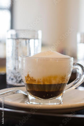 Caffè schiumato in tazza di vetro servito in un bar con accompagnato un bicchiere d'acqua frizzante