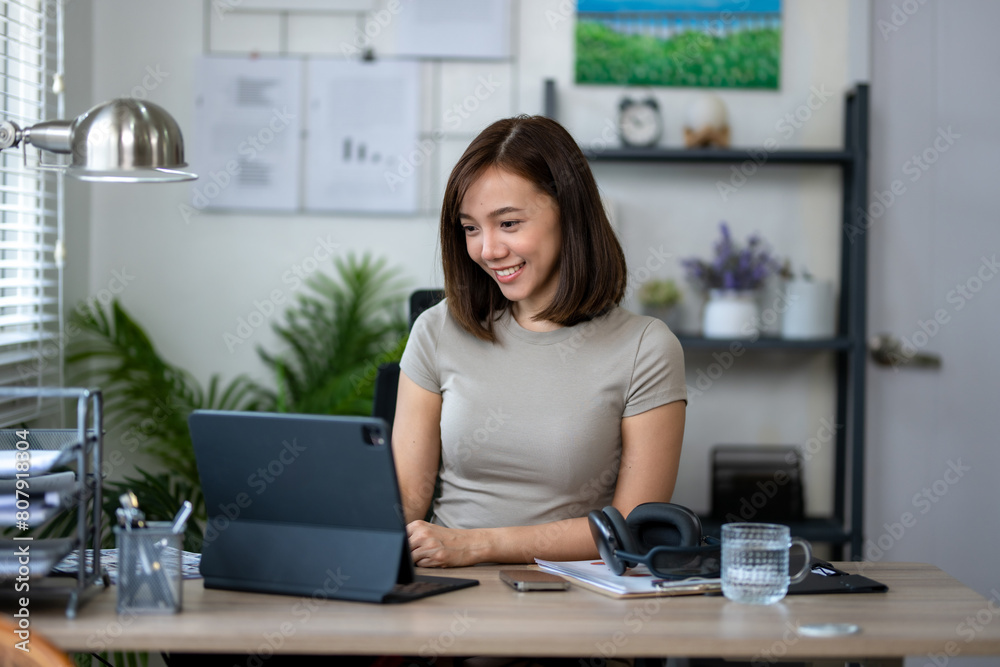 A woman is sitting at a desk with a laptop and a tablet. She is smiling and she is enjoying her work A woman is sitting at a desk with a laptop and a tablet. She is smiling and she is enjoying her work