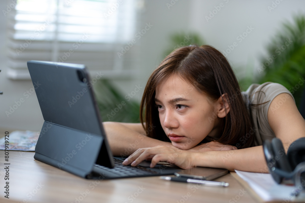 A woman is laying on a desk with a laptop in front of her. She is looking at the screen with a frown on her face A woman is laying on a desk with a laptop in front of her. She is looking at the screen with a frown on her face