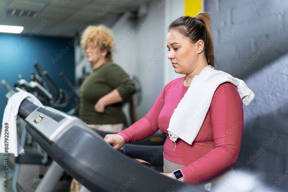 Two beautiful, overweight women power through a fitness routine, determined to achieve their goals. Workout on the treadmill. Two beautiful, overweight women power through a fitness routine, determined to achieve their goals. Workout on the treadmill.