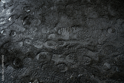 Black sand texture with shoe footprints. Wet volcanic soil, traces of human passage. Reflections of light, water, beach, mud. photo