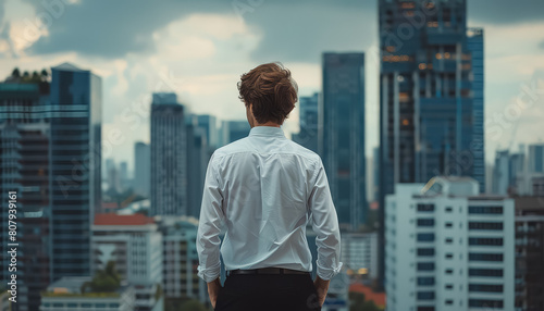 A man in a white shirt stands on a rooftop looking out over a city