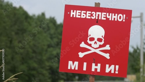 A red warning sign with an inscription is mined against the background of a green forest. The concept of humanitarian demining. Consequences of hostilities. Russian-Ukrainian war. photo