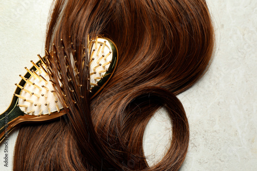 Stylish brush with brown hair strand on grey table, top view