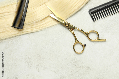 Professional hairdresser scissors and comb with blonde hair strand on grey table, top view. Space for text