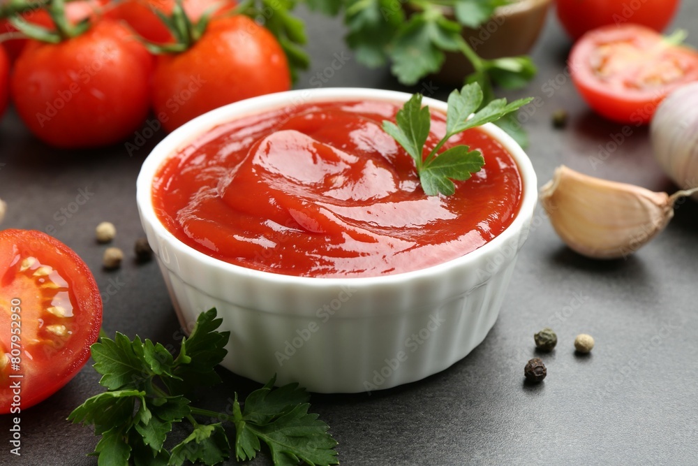 Delicious ketchup in bowl, tomatoes, parsley and garlic on grey table, closeup Delicious ketchup in bowl, tomatoes, parsley and garlic on grey table, closeup