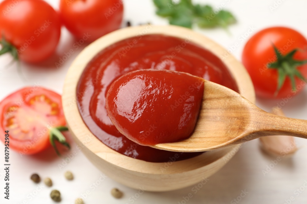 Taking delicious tomato ketchup with spoon from bowl at white table, closeup Taking delicious tomato ketchup with spoon from bowl at white table, closeup