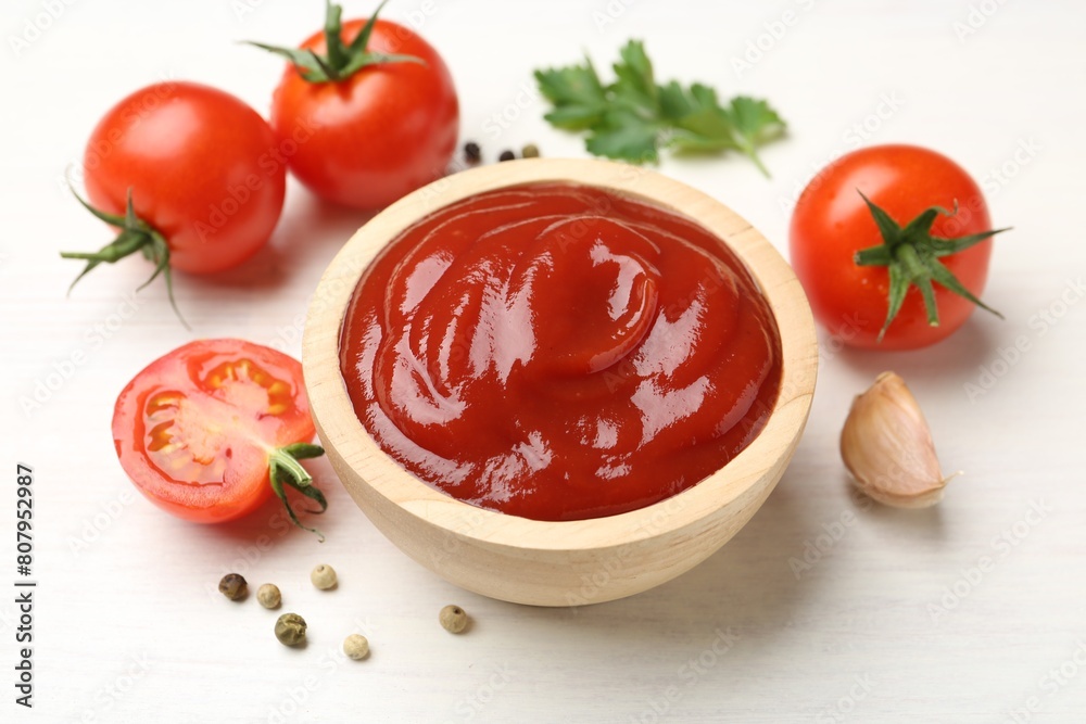 Delicious ketchup in bowl, garlic and tomatoes on white wooden table, closeup Delicious ketchup in bowl, garlic and tomatoes on white wooden table, closeup