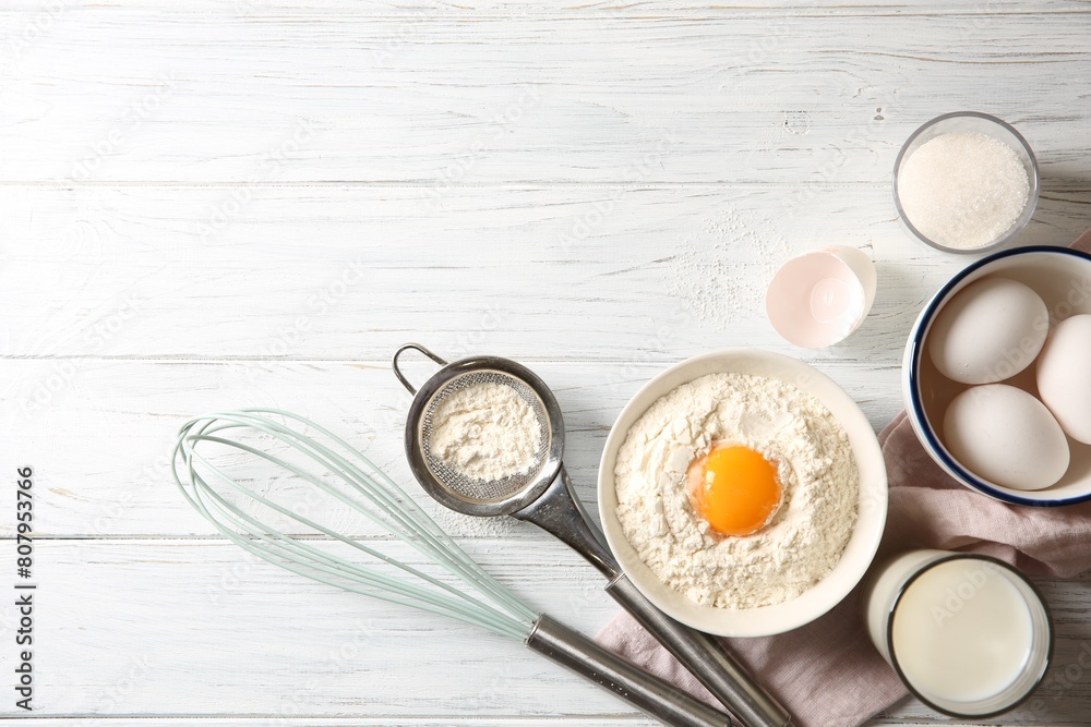 Flour with yolk in bowl and other ingredients for dough on white wooden table, flat lay. Space for text Flour with yolk in bowl and other ingredients for dough on white wooden table, flat lay. Space for text