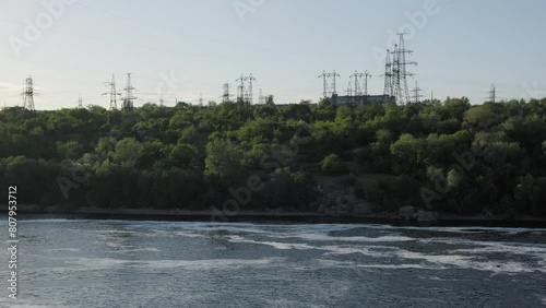 Powering the Riverbanks: Electricity Infrastructure along the Dnipro in Zaporizhzhia. Power grid infrastructure combined with nature. Electric Supports on the slopes of the river. photo