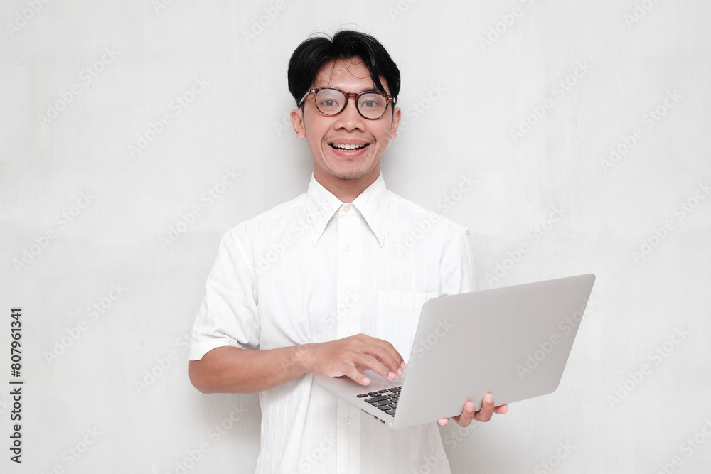 Portrait man in glasses smiling happily holding laptop looking at camera, wearing white shirt isolated Portrait man in glasses smiling happily holding laptop looking at camera, wearing white shirt isolated