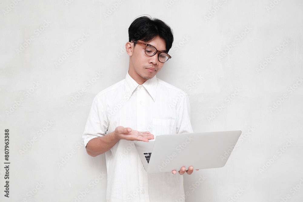 Young white shirt man pointing at laptop with disappointed expression isolated on white background. Young white shirt man pointing at laptop with disappointed expression isolated on white background.