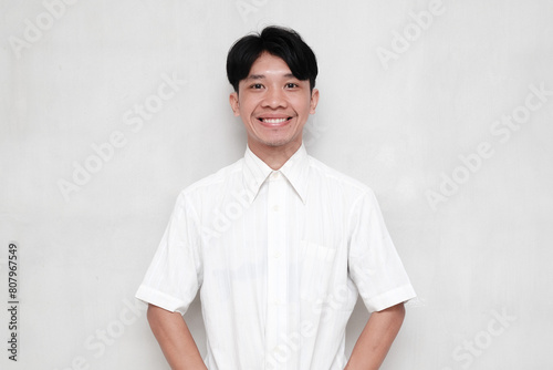 Asian young man wearing white shirt smiling cheerfully against isolated background photo