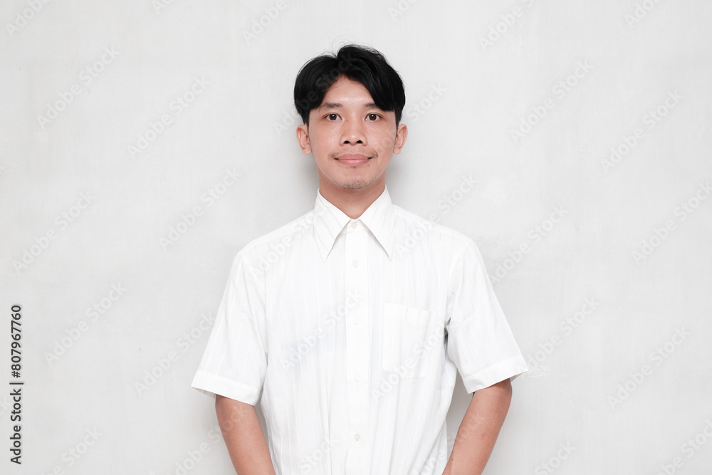 Asian young man wearing a white shirt smiling thinly against an isolated background Asian young man wearing a white shirt smiling thinly against an isolated background