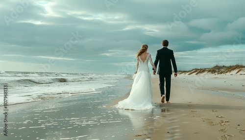 A bride and groom are walking on the beach, hand in hand