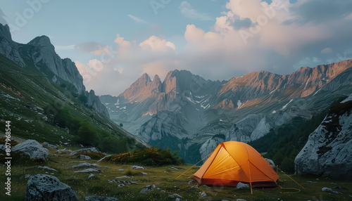 A small orange tent is set up in a grassy field with mountains in the background © terra.incognita