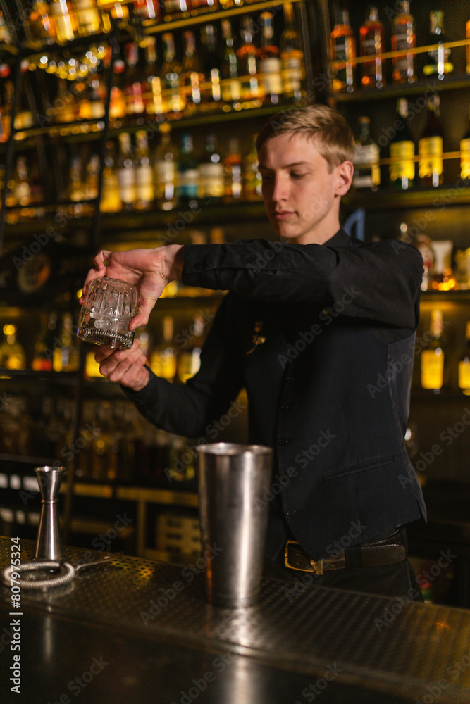 Bartender uses strainer to sieve large pieces of ice before pouring cocktail into pub clients glass. Barkeeper professionally fulfills order for cocktails