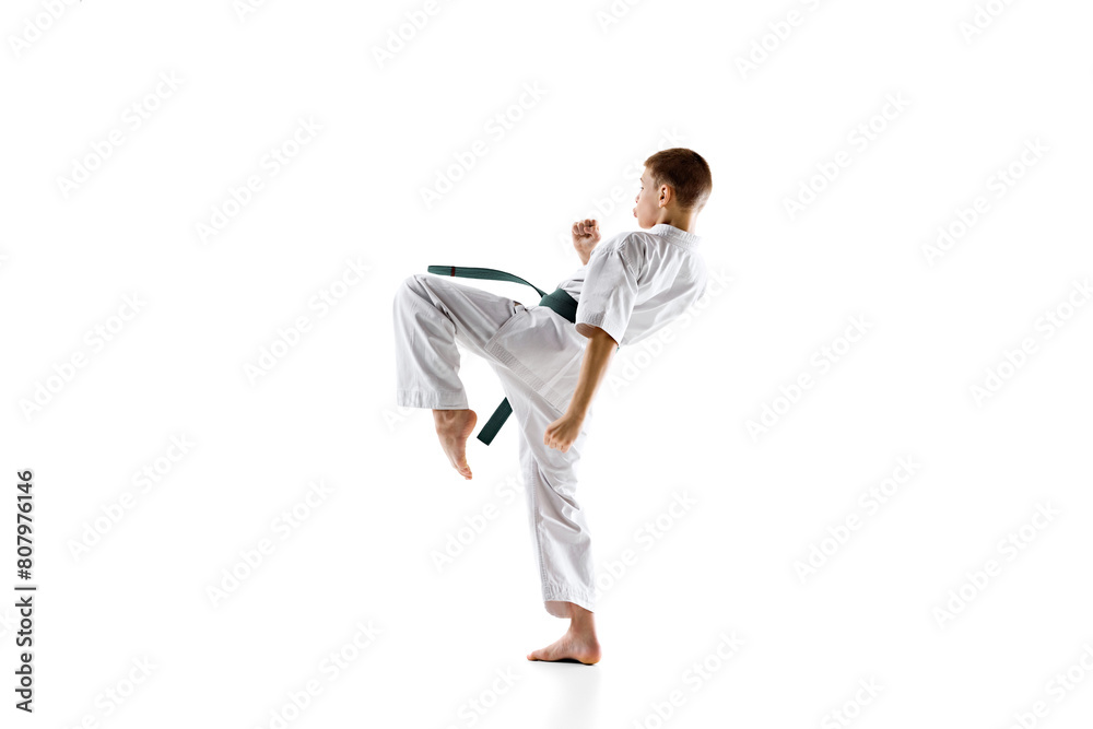 Karate student in white kimono and green belt, in motion, performing powerful kick during practice session, isolated on white background. Concept of sport, martial arts, combat sport, active lifestyle Karate student in white kimono and green belt, in motion, performing powerful kick during practice session, isolated on white background. Concept of sport, martial arts, combat sport, active lifestyle