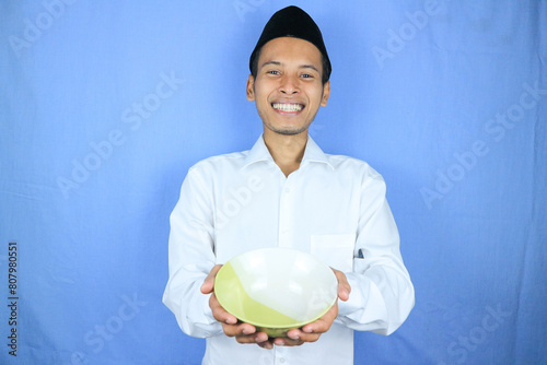 Muslim asian man wearing a cap stand and hold an empty bowl and spoon showing the dish photo