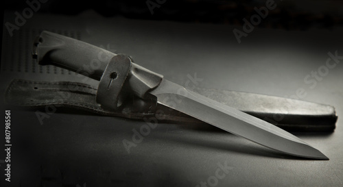 .a black travel knife and a leather sheath on a black background. There are drops of water on the surface