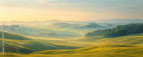 The early morning sun bathes rolling hills in a warm, golden glow, highlighting the tranquil beauty of the lush countryside landscape at dawn.