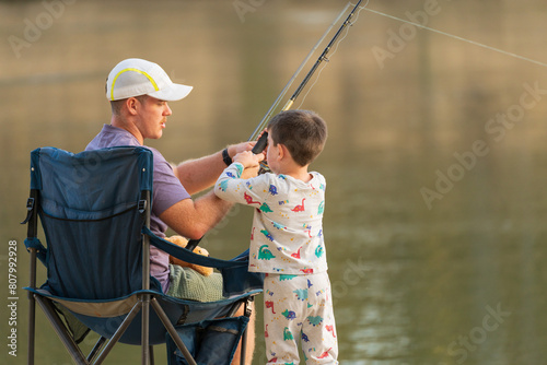 Rear view of a man and a young boy fishing together on a river bank photo