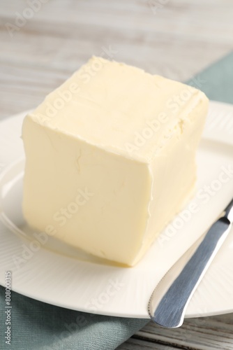 Block of tasty butter and knife on white wooden table, closeup
