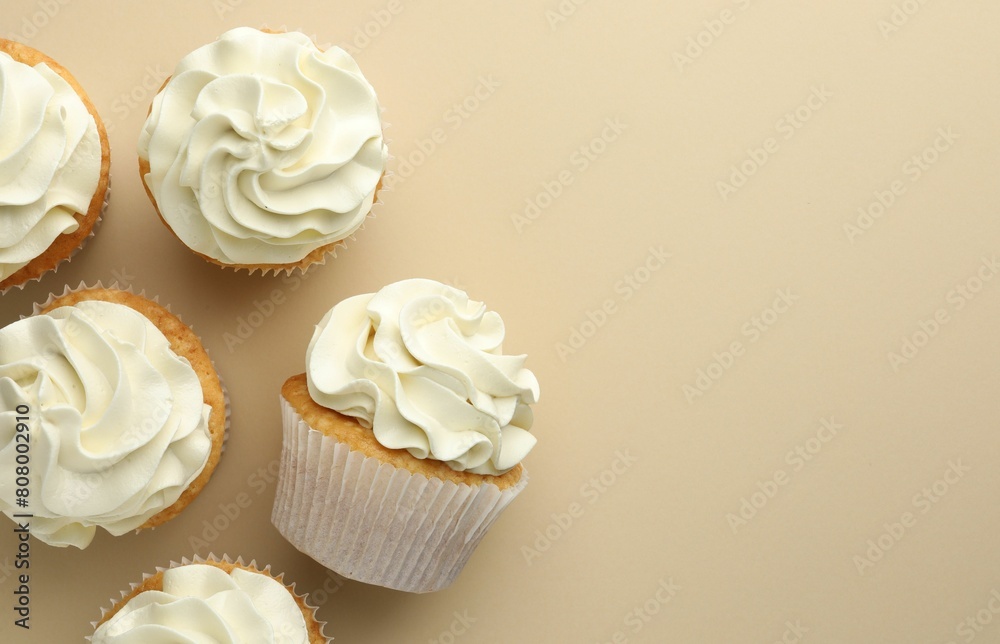 Tasty vanilla cupcakes with cream on beige background, top view. Space for text Tasty vanilla cupcakes with cream on beige background, top view. Space for text