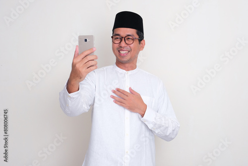 Moslem Asian man smiling happy while video call using his mobile phone photo