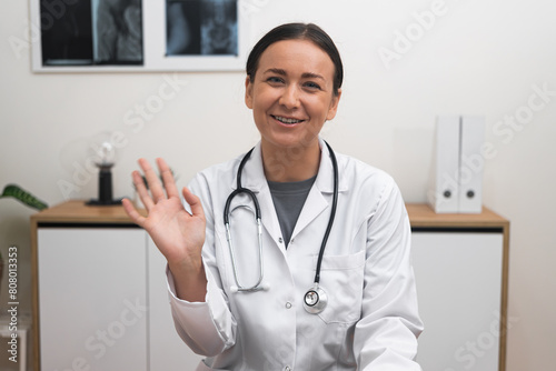 Online Consultation Welcome: With a welcoming smile, a female doctor waving hand engages with the camera, making patients feel comfortable during their online appointment. 