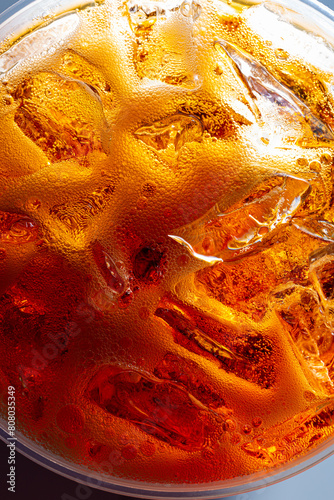 Cola drink surface close-up, top view,Close up view of the ice cubes in dark cola background. Texture of cooling sweet summer's drink with foam and macro bubbles on the glass wall.