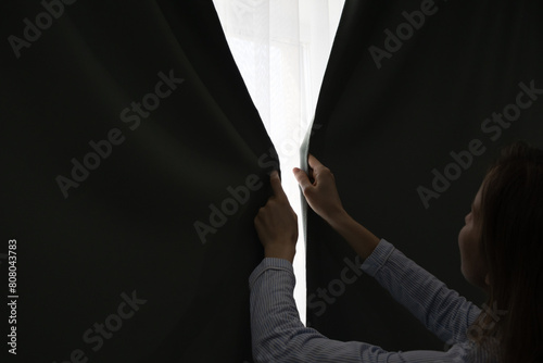 Woman is closing curtains near the window. Sunny day. Sunshine and warm at home.