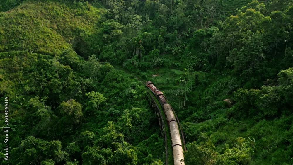 Train winds through Sri Lankan mountains near Ella at sunrise. Aerial shot scenic railroad journey in plants. Early morning bathes tropical landscape, eco-tourism, adventure travel.