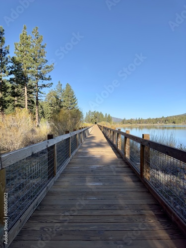 A wooden boardwalk winds along a serene mountain lake  framed by towering peaks. The bridge invites a leisurely stroll  offering breathtaking views of the tranquil waters and rugged landscape.