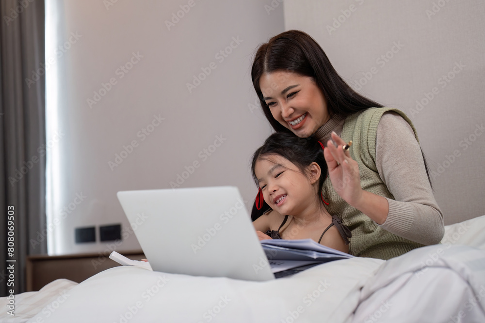 Mother and daughter lying in bed with on and smiling. Young mom working from home in bedroom with laptop Mother and daughter lying in bed with on and smiling. Young mom working from home in bedroom with laptop