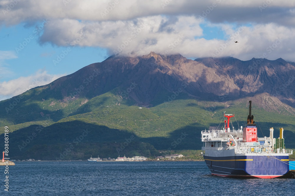 Japanese cargo, passenger and car ferry with Sakurajima volcano and picturesque coastal scenery in Kagoshima, Japan on sunny afternoon