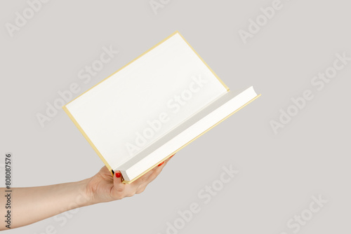 Closeup of woman hand showing open paper organizer with empty pages, copy space for promotion. Indoor studio shot isolated on gray background.