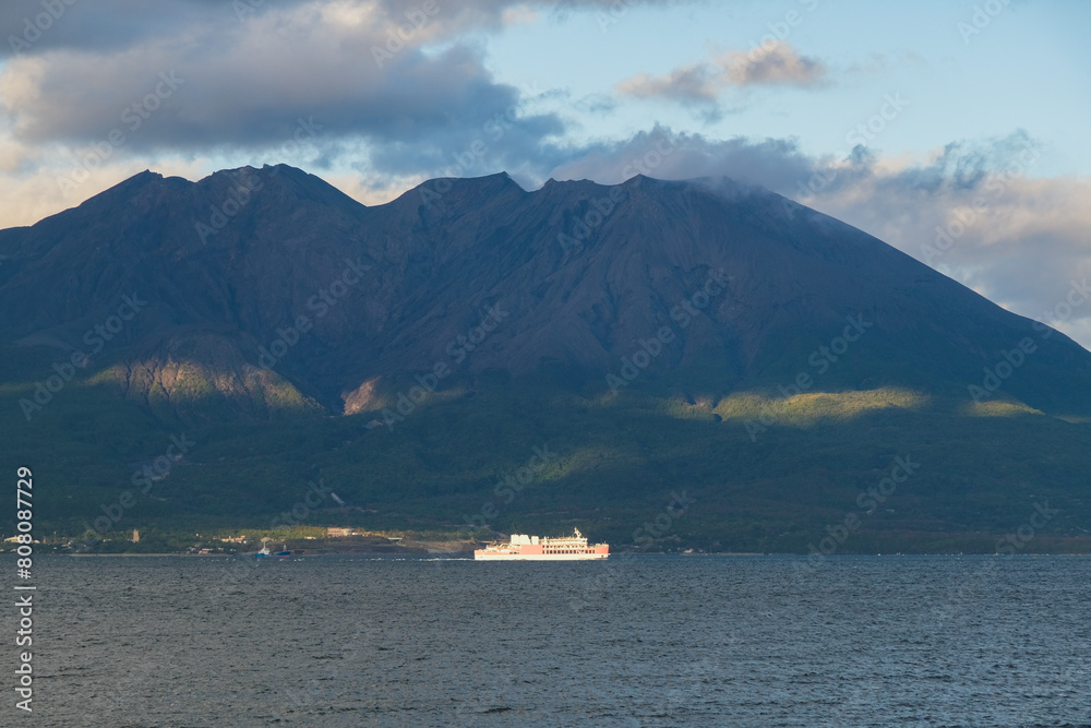Japanese cargo, passenger and car ferry with Sakurajima volcano and picturesque coastal scenery in Kagoshima, Japan on sunny afternoon