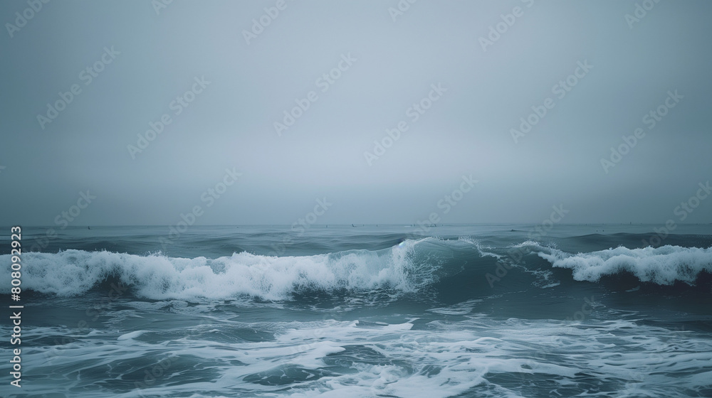 This atmospheric photograph captures the captivating allure of ocean waves under a brooding sky. The tumultuous waves roll and crash against the shoreline, their frothy crests illuminated by the faint