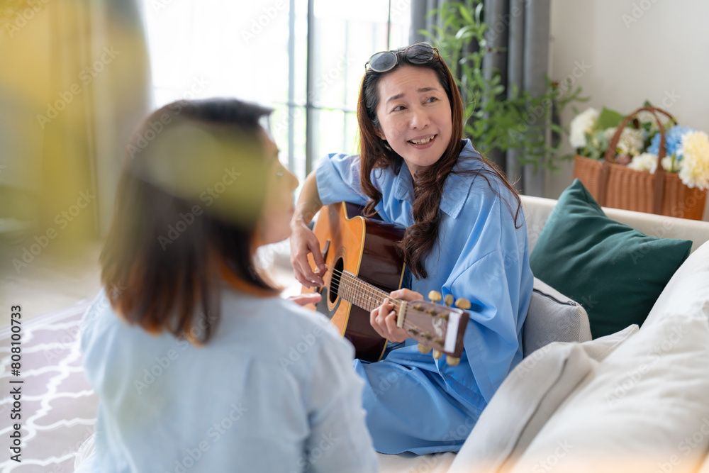 Obraz premium asian adult woman friend gathering having fun together while singing and playing the guitar at home. Friendship, reunion fun party home entertainment and people celebrate festive concept