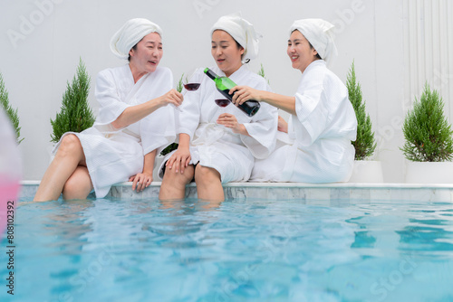 chilling sunday pool party asian adult friend woman in bathrope casual cloth hanging around sit near water pool hand hold glass wine enjoy conversation old friend meeting laugh smile carefree summer