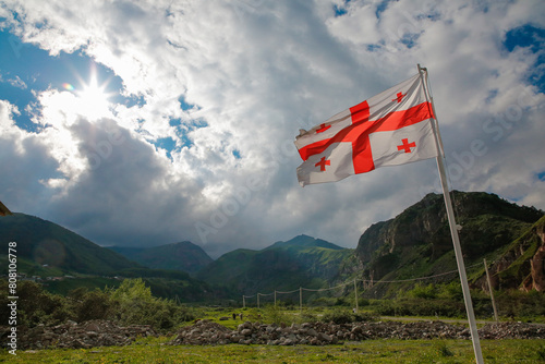 Georgian Flag Waving Proudly Under Sunlit Cloudy Sky with Mountainous Backdrop