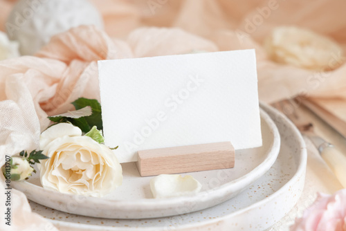 Card near cream tulle fabric on plates close up, copy space, wedding stationery mockup