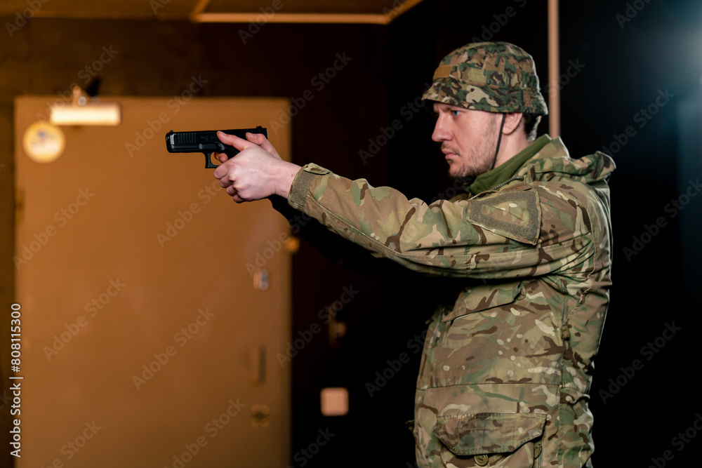 Fototapeta premium In a professional shooting range a military man in ammunition takes aim from a cleaned pistol