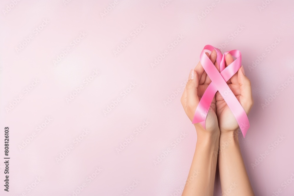 The image shows the hands of a person holding a pink ribbon. The pink ribbon is a symbol of breast cancer awareness. The image is taken from a top view. The image shows the hands of a person holding a pink ribbon. The pink ribbon is a symbol of breast cancer awareness. The image is taken from a top view.