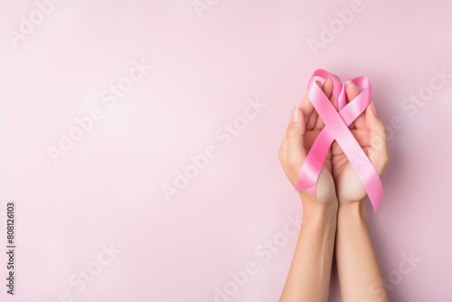 The image shows the hands of a person holding a pink ribbon. The pink ribbon is a symbol of breast cancer awareness. The image is taken from a top view.