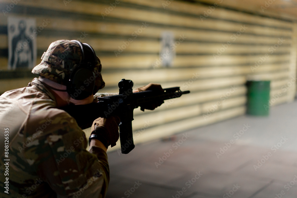 Fototapeta premium In a professional shooting range military man in ammunition makes a shot from a NATO rifle