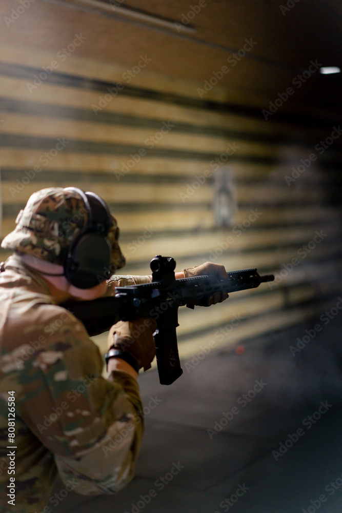 Fototapeta premium In a professional shooting range military man in ammunition makes a shot from a NATO rifle