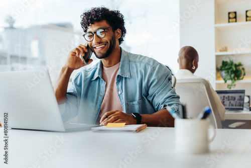 Happy young entrepreneur speaking on smartphone at modern office workplace